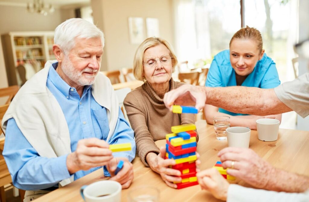 A group of seniors playing a game of Jenga while a caregiving staff member joins them in the game.