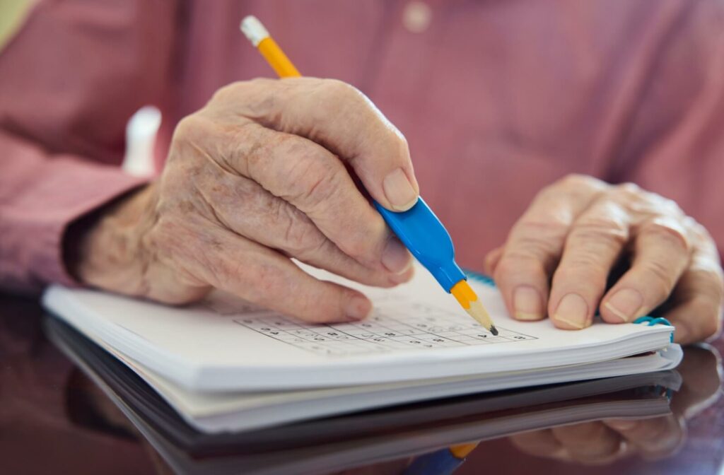 An older adult writes in a puzzle book to help keep their mind sharp.