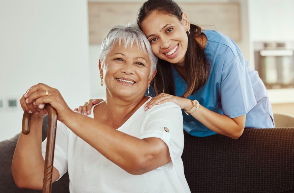 A caregiver and an older adult smile together on the couch in a home in senior living