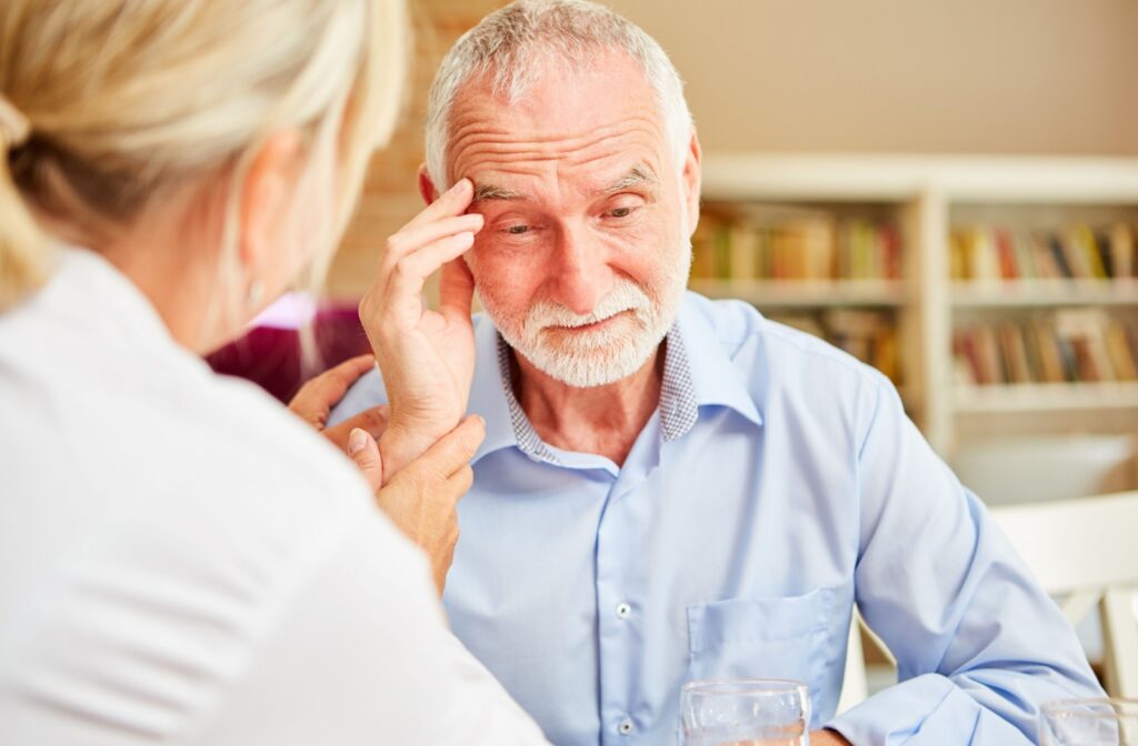A caregiver gently holds the hand of an elderly person looking down in confusion