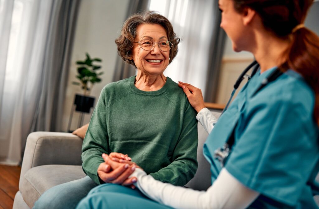 An older adult smiles while a caregiver touches their hand during a seated conversation after a checkup in memory care