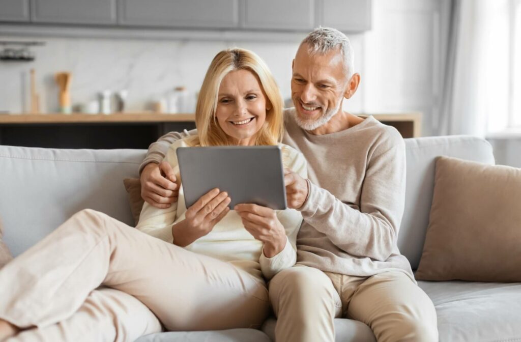An older couple research senior living options on a tablet together while cuddling on the couch
