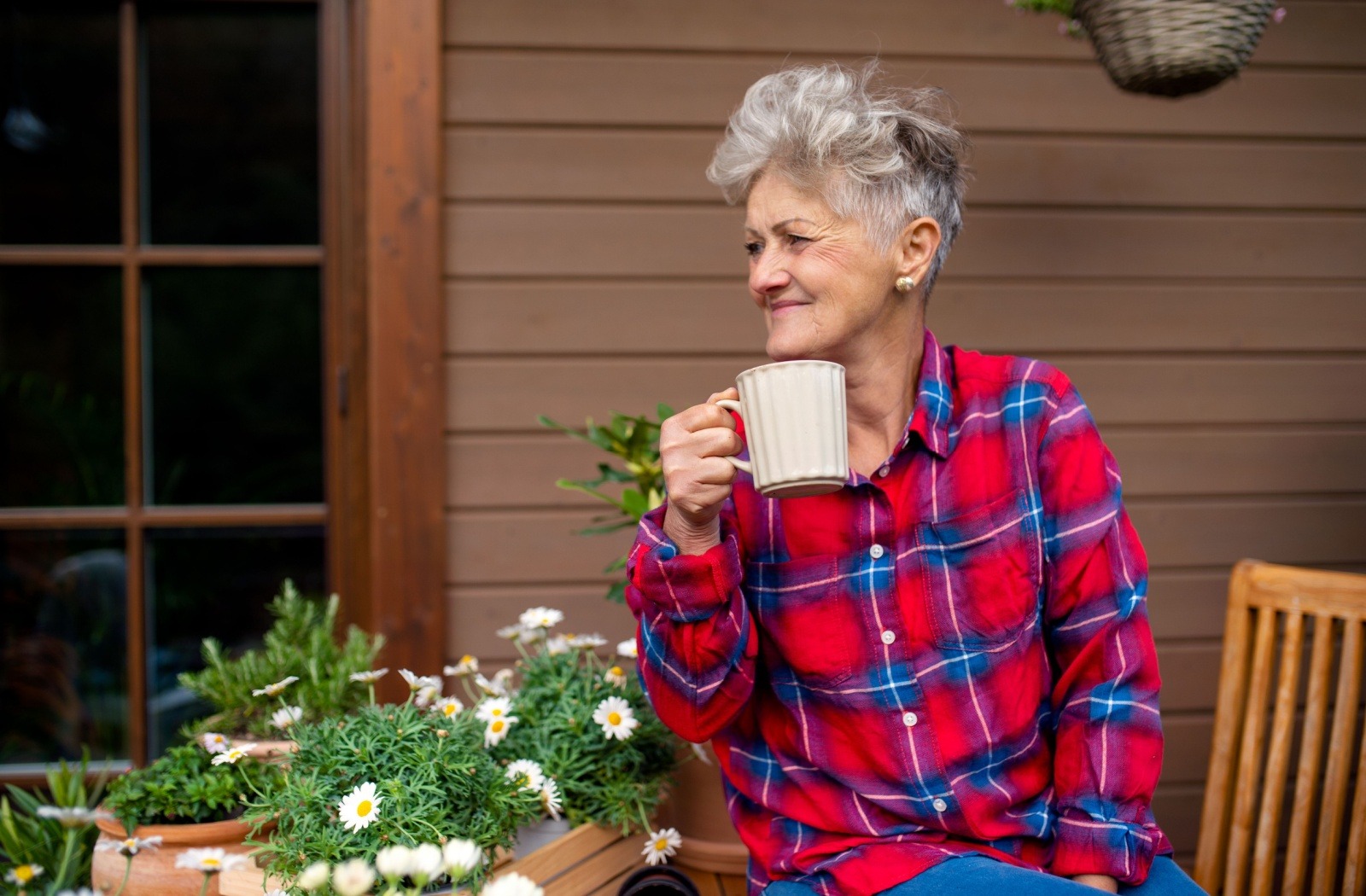 An older adult enjoys a cup of coffee on a sunlit porch.