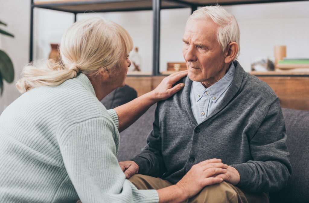 An older adult gently touches their spouse's shoulder and holds their hand to comfort them.